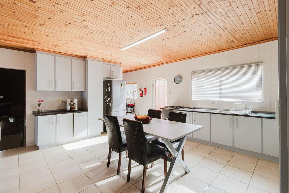 A functional kitchen featuring light-toned cabinetry, laminate countertops, a gas hob, and a distinctive timber-clad ceiling with tiled flooring throughout.