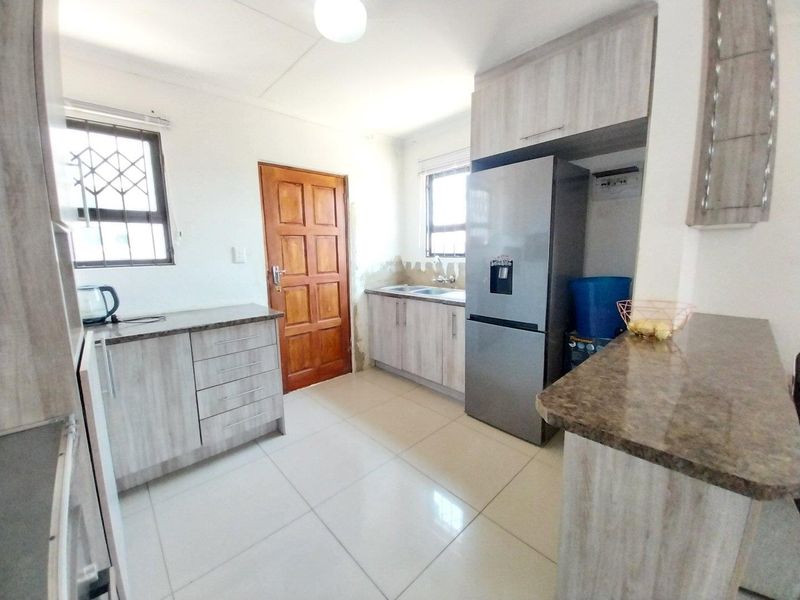 A functional kitchen featuring light wood-grain cabinetry, stone-look laminate countertops, tiled flooring, and security-fitted windows.