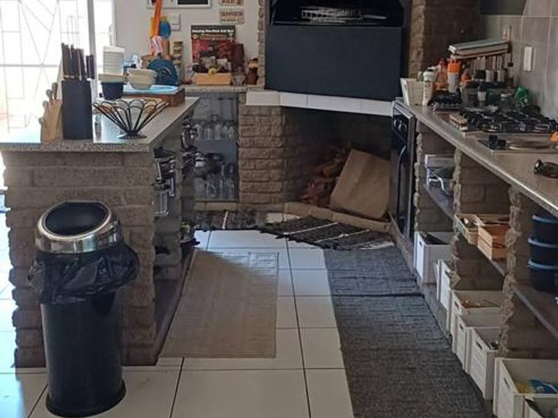 A functional kitchen featuring a prominent built-in brick braai, tiled flooring, and stone-topped counters with integrated shelving for storage.