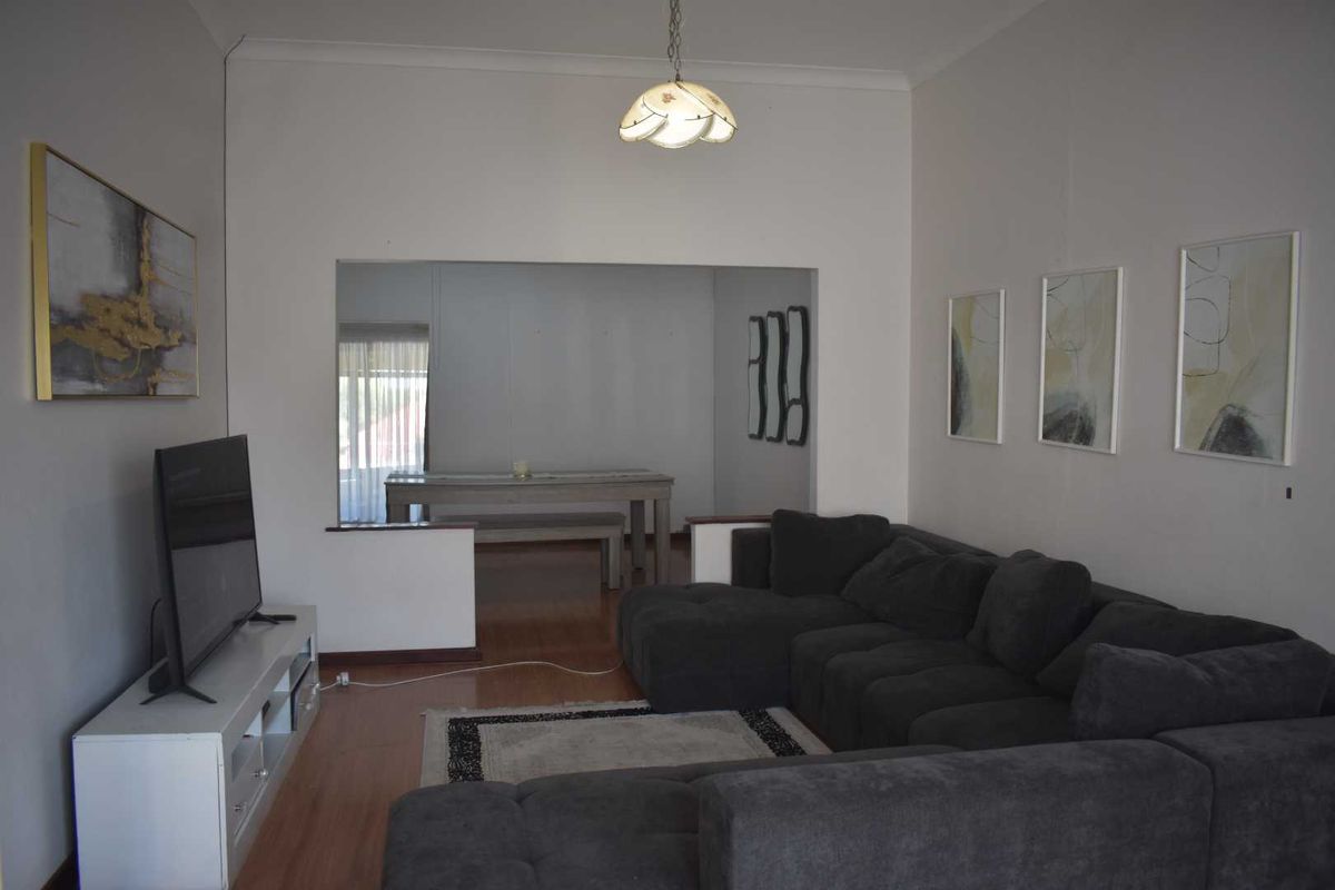 A living room featuring laminate flooring and a pass-through opening to an adjacent dining area, providing an open-plan feel.
