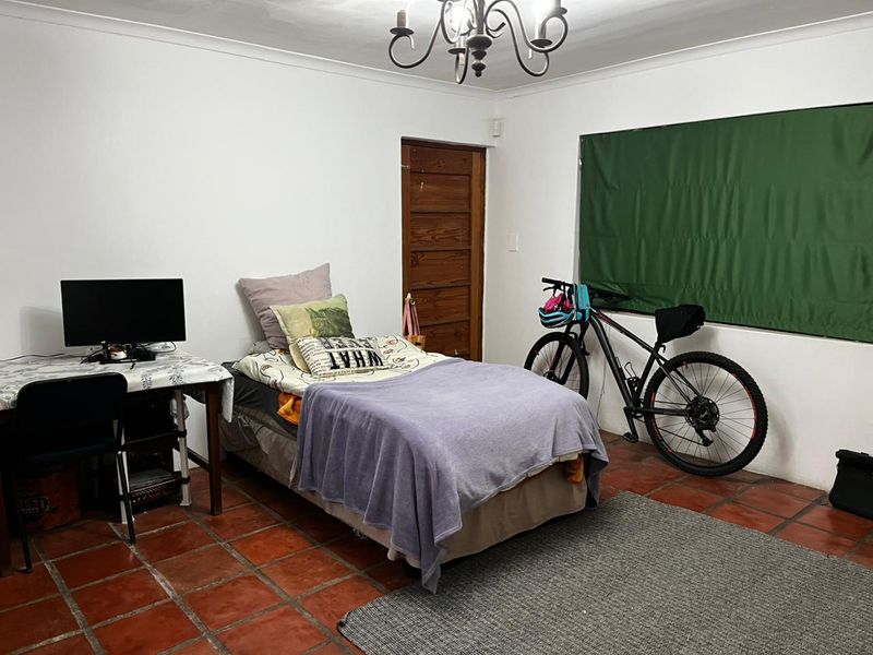 A bedroom featuring terracotta floor tiles, a timber door, and a wrought iron chandelier, offering a functional space with potential for cosmetic updates.