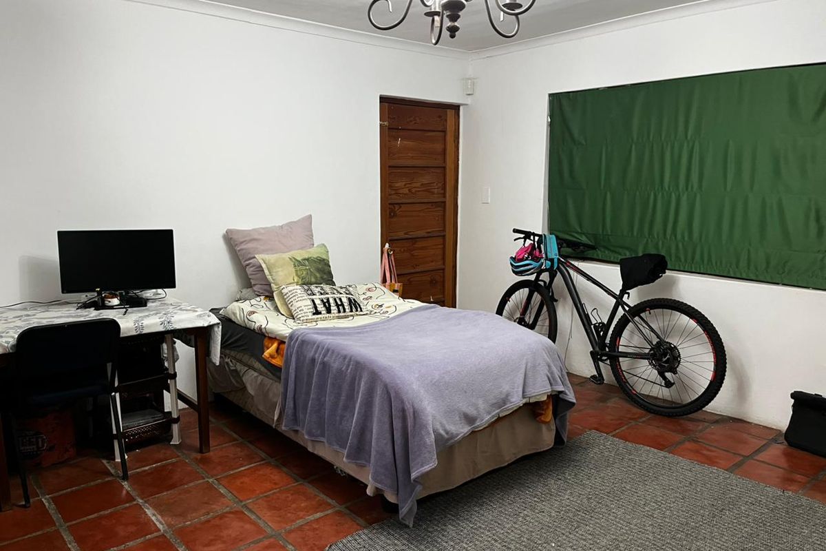 A bedroom featuring terracotta floor tiles, a timber door, and a wrought iron chandelier, offering a functional space with potential for cosmetic updates.
