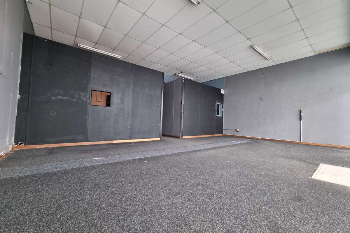An empty open-plan commercial space featuring dark partition walls, carpeted flooring, and a suspended ceiling with integrated fluorescent lighting.