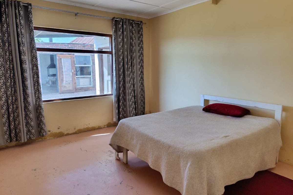 A spacious bedroom featuring large windows, painted concrete flooring, and neutral wall finishes, offering a blank canvas for potential renovation and modernization.