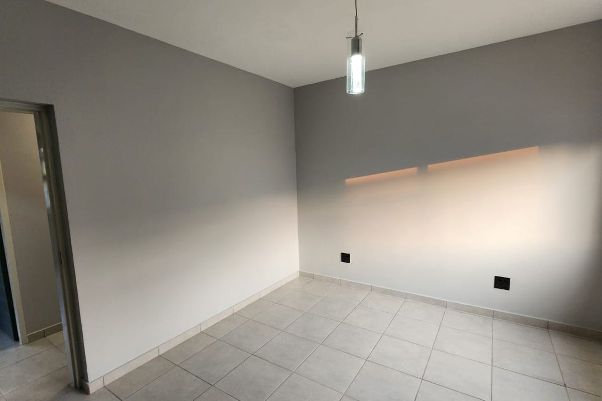A clean, empty bedroom featuring neutral grey walls, tiled flooring, and a modern pendant light fixture, ready for personalization.