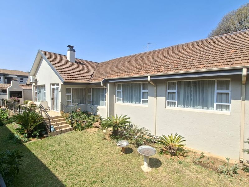 Rear view of the townhouse featuring a tiled roof, built-in braai area, and a private garden with established landscaping.