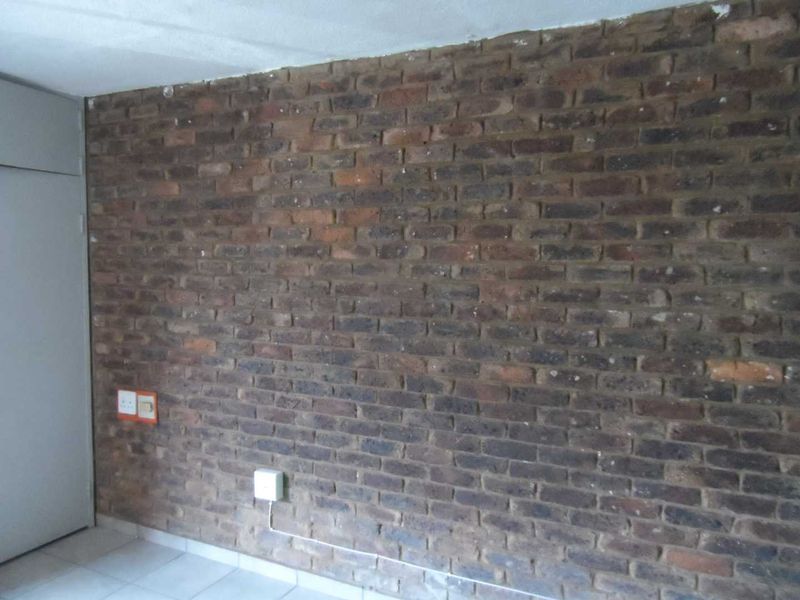 An empty bedroom featuring an exposed brick feature wall, tiled flooring, and a built-in cupboard, offering a blank canvas for renovation.