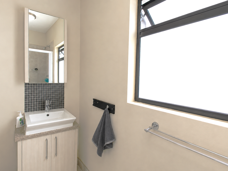 A modern bathroom featuring a vanity cabinet with a basin, tiled splashback, wall-mounted mirror, and an aluminium-framed window.
