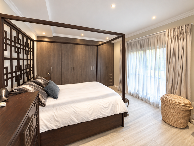 Spacious bedroom featuring extensive built-in wooden cabinetry, modern laminate flooring, recessed lighting, and large sliding doors with floor-to-ceiling curtains.