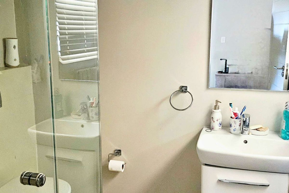 A functional bathroom featuring a wall-mounted vanity with basin, a glass-enclosed shower, and a wall-mounted toilet with a concealed cistern.