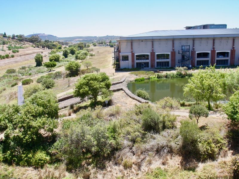 An elevated view overlooking a landscaped area with a pond and adjacent commercial building structure.