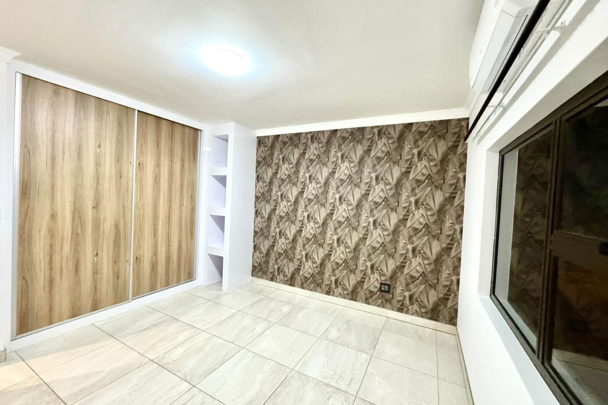 A clean, empty bedroom featuring tiled floors, a built-in wardrobe, integrated shelving, and a decorative feature wall with an installed air conditioning unit.