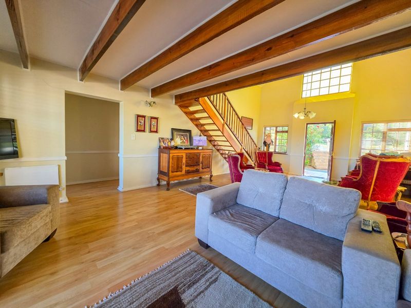 Spacious living room featuring exposed timber ceiling beams, a wooden staircase, and laminate flooring, with natural light flowing from the rear entrance.