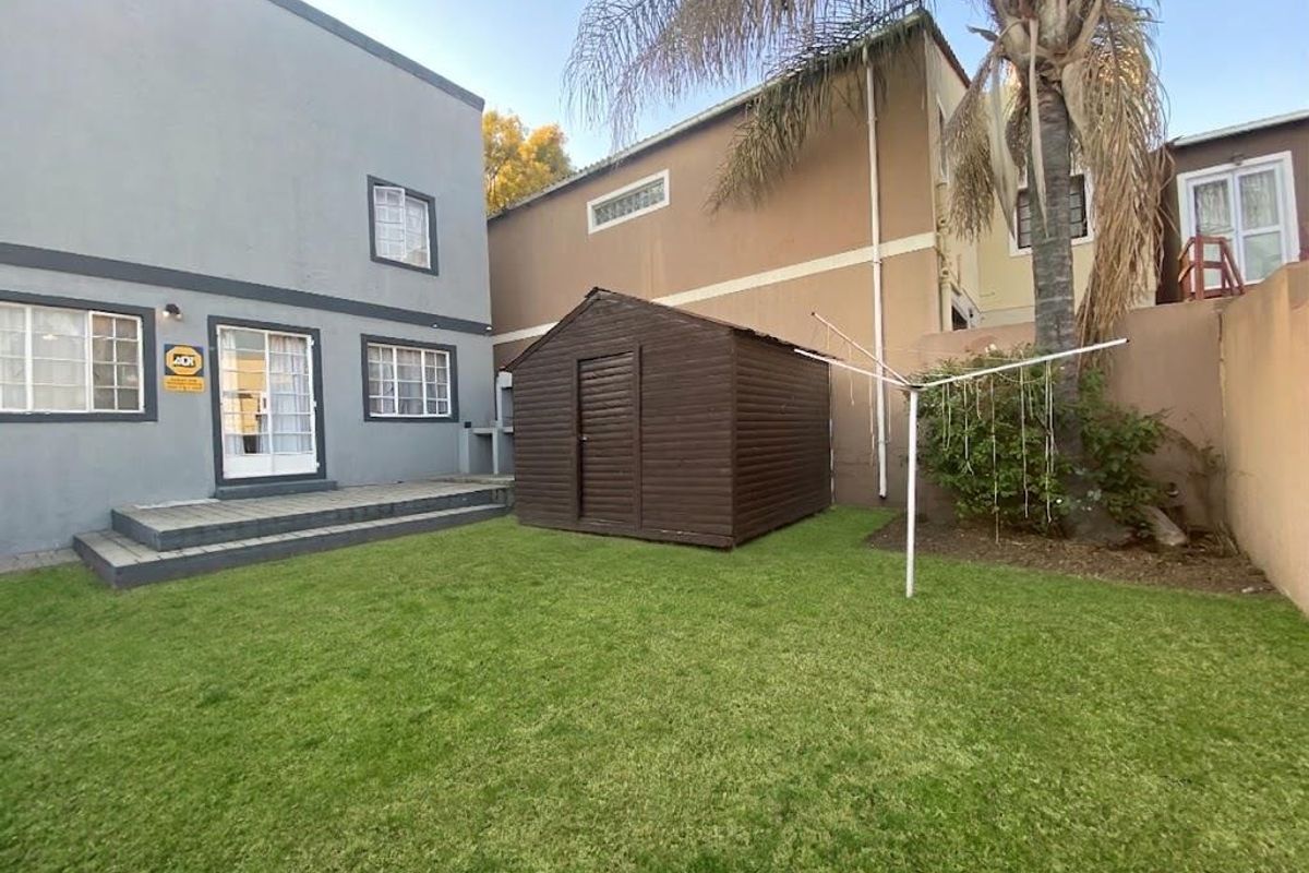A rear garden area featuring a small lawn, paved patio section, and boundary walls, providing a private outdoor space for the townhouse.