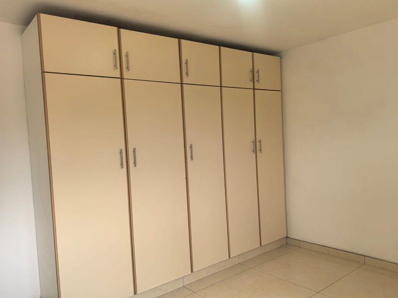 A clean, empty bedroom featuring neutral tiled flooring and extensive floor-to-ceiling built-in cupboards for ample storage.