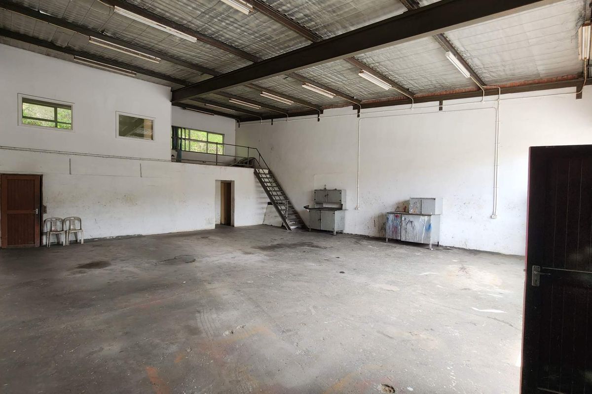 Spacious industrial utility area featuring high ceilings, exposed steel beams, a mezzanine level with staircase access, and concrete flooring suitable for workshop or storage use.