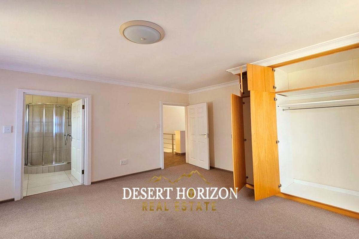 Spacious bedroom featuring built-in wooden cabinetry, neutral carpeting, and direct access to an en-suite bathroom.