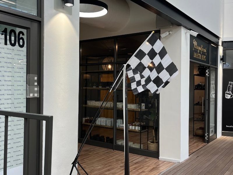 Modern retail storefront entrance featuring timber decking, black metal-framed glass doors, and contemporary wall-mounted lighting.