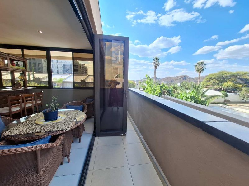 A spacious covered balcony featuring tiled flooring, aluminium glass doors, and a built-in bar area, offering scenic outdoor views.