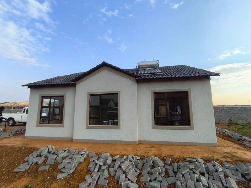Front elevation of a modern single-story house featuring a tiled roof, solar water heater, and aluminium window frames, currently undergoing final exterior site works.