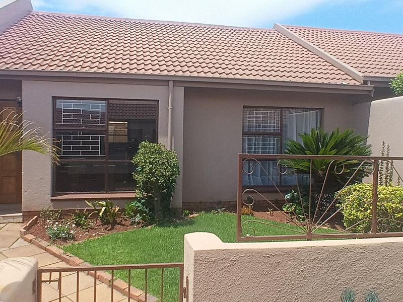 Front view of a townhouse featuring a tiled roof, paved walkway, and a small private garden enclosed by a boundary wall and metal gate.