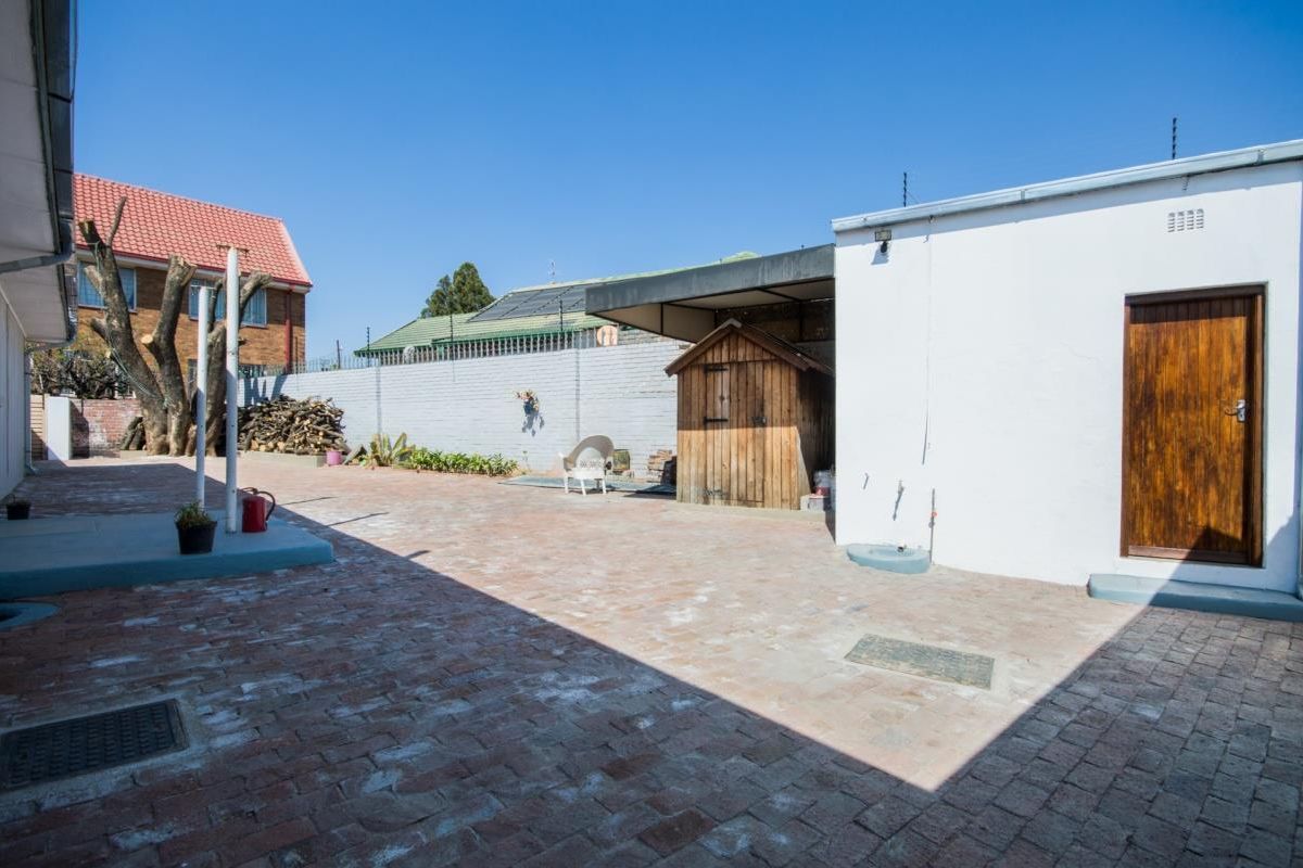 A paved rear courtyard area featuring a brick boundary wall, a small wooden storage structure, and a solid timber door entrance.
