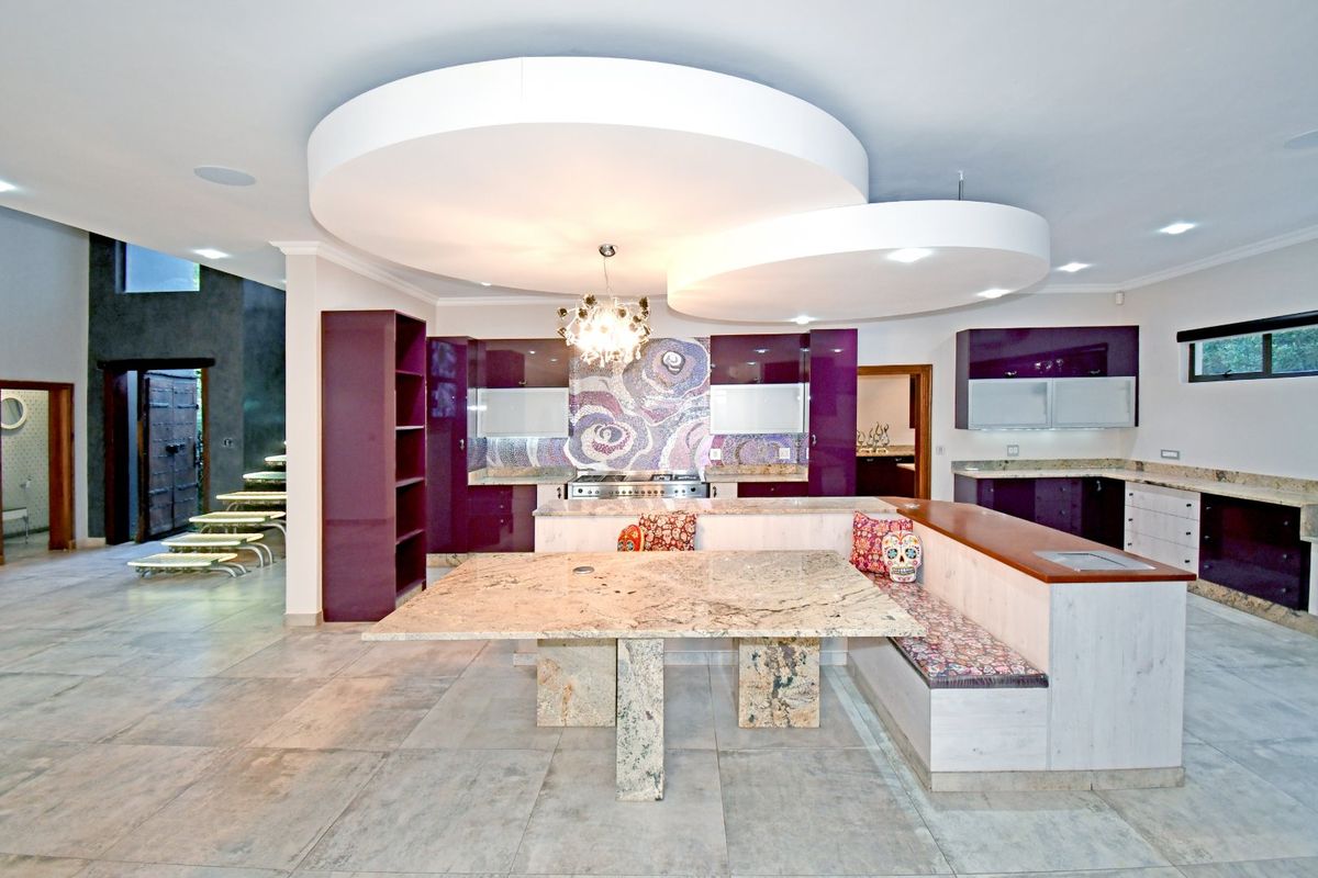 Spacious kitchen featuring high-gloss purple cabinetry, granite countertops, a unique mosaic backsplash, and a built-in breakfast nook under a modern circular ceiling feature.