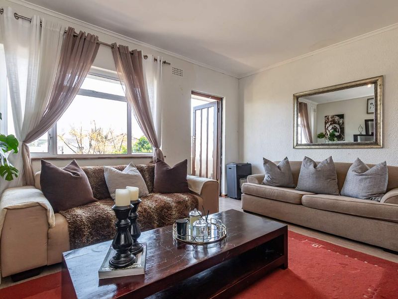 A comfortable living room featuring neutral walls, cornicing, and natural light through aluminium-framed windows, with direct access to an outdoor area.