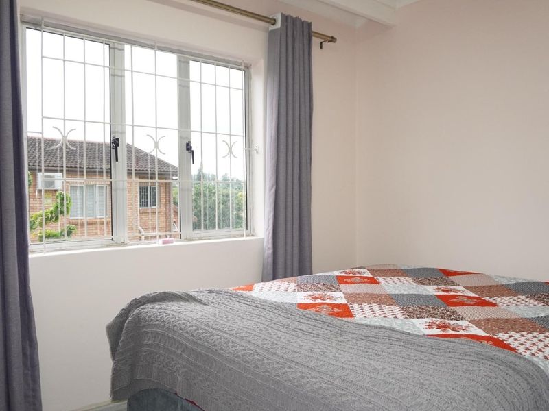 A bedroom featuring a window with fitted security bars and curtain rods, providing natural light and a view of the surrounding residential area.