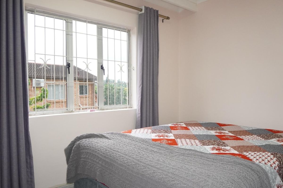A bedroom featuring a window with fitted security bars and curtain rods, providing natural light and a view of the surrounding residential area.