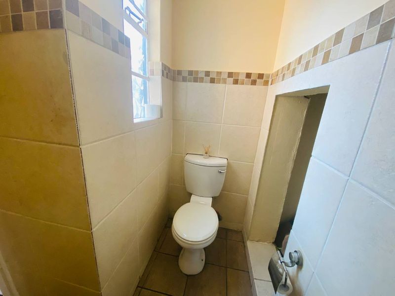 A compact guest bathroom featuring tiled walls with a decorative border, a standard toilet, and a small window for natural light.