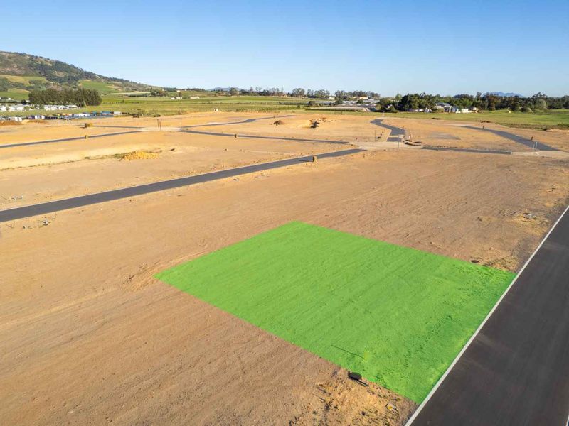 An aerial view of a vacant residential plot in a developing estate, featuring paved road access and clear boundaries.