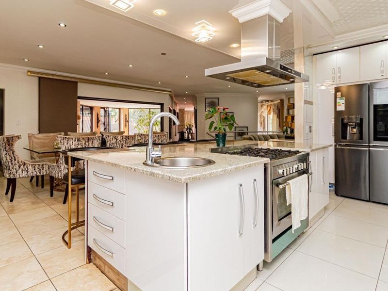Spacious open-plan kitchen featuring a central island with granite countertops, gas hob, stainless steel extractor, and modern tiled flooring throughout.