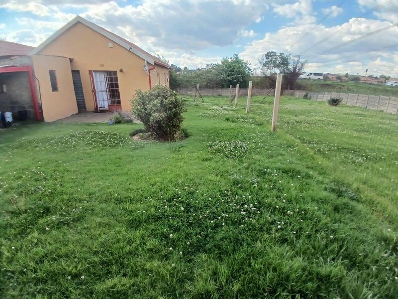 Rear view of the property featuring a large, open garden area with a concrete boundary wall and direct access to the home.