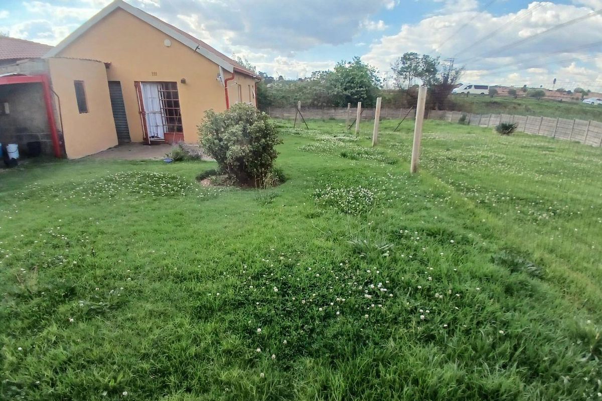 Rear view of the property featuring a large, open garden area with a concrete boundary wall and direct access to the home.