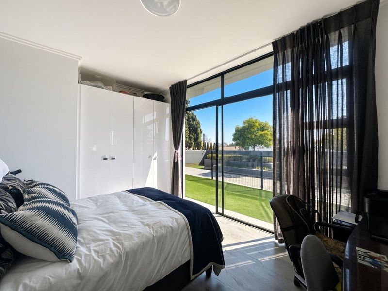 Bright bedroom featuring built-in wardrobes, modern laminate flooring, and large sliding glass doors providing direct access to an outdoor patio area.