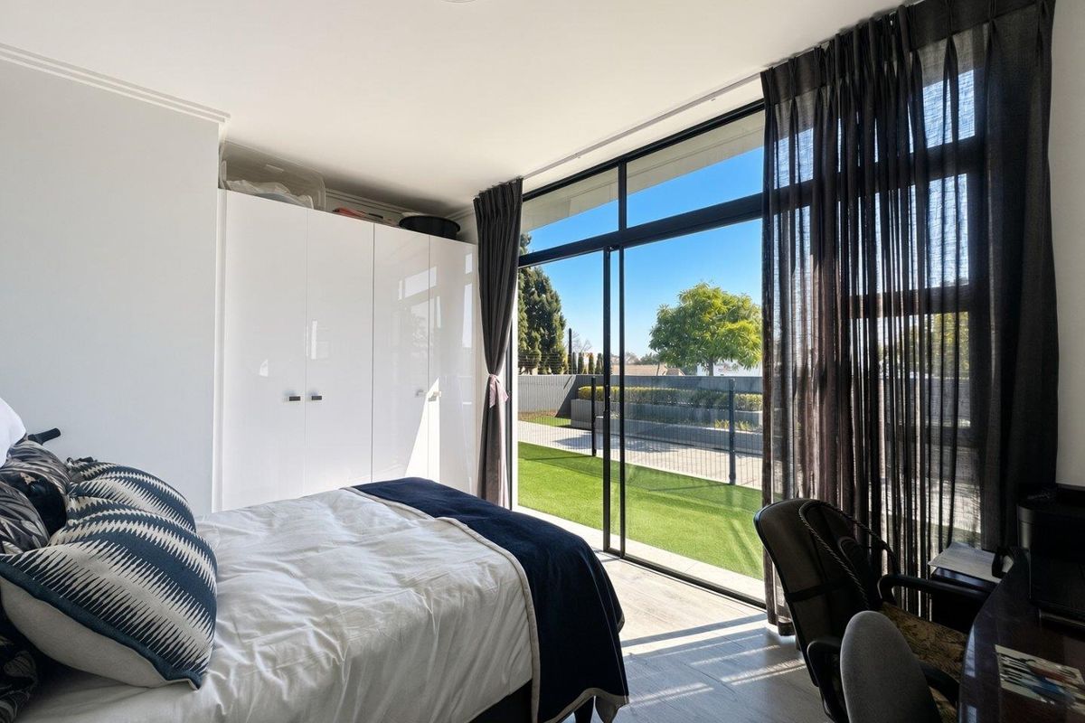 Bright bedroom featuring built-in wardrobes, modern laminate flooring, and large sliding glass doors providing direct access to an outdoor patio area.