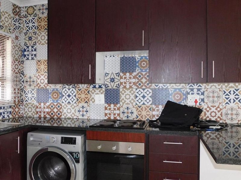 A functional kitchen featuring dark wood cabinetry, granite countertops, and a decorative patterned tile backsplash with integrated oven and hob.