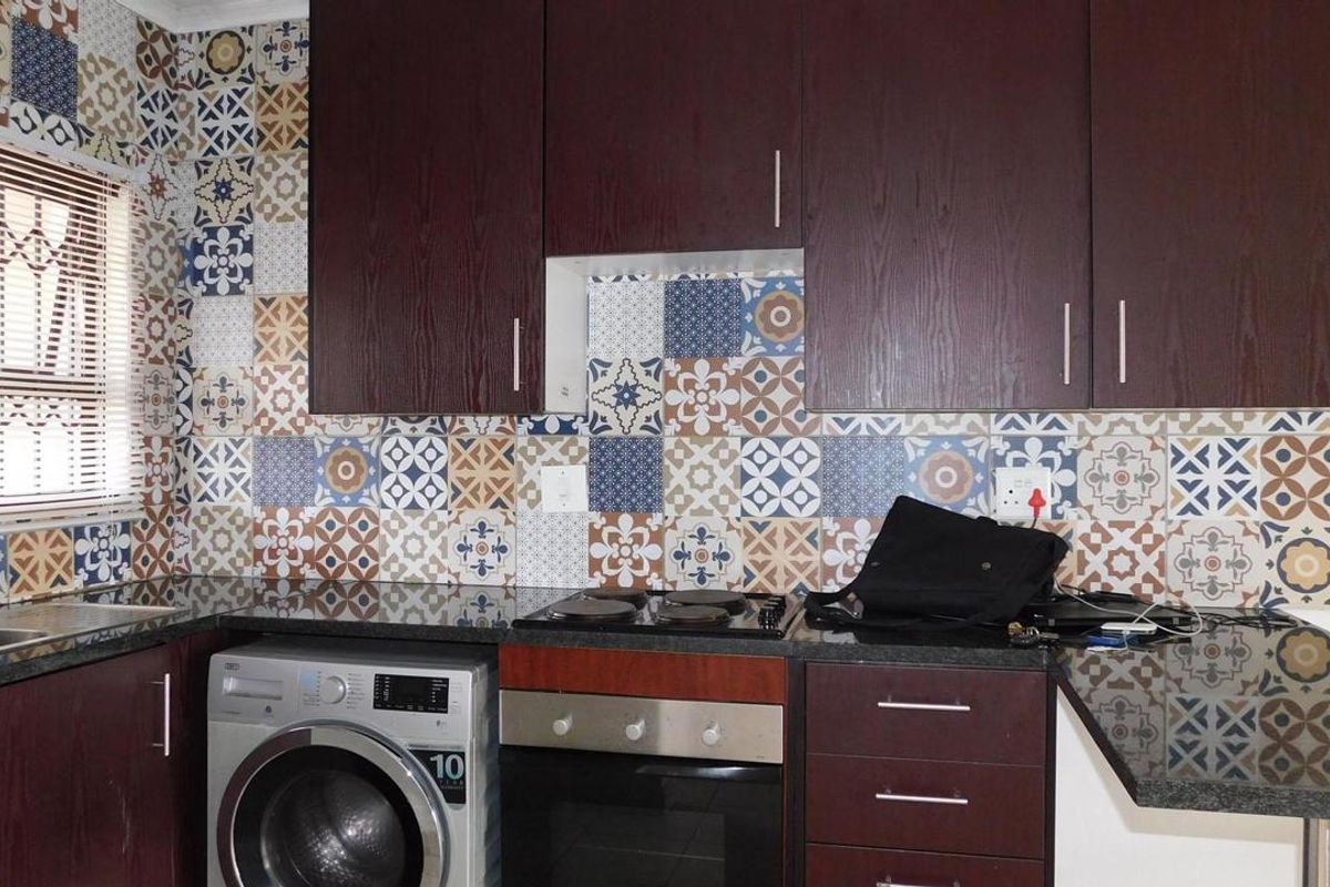 A functional kitchen featuring dark wood cabinetry, granite countertops, and a decorative patterned tile backsplash with integrated oven and hob.