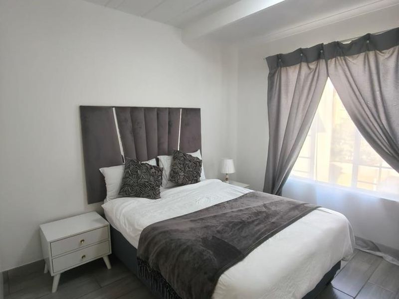 A well-maintained bedroom featuring modern grey floor tiles, a neutral color palette, and a large window allowing for natural light.