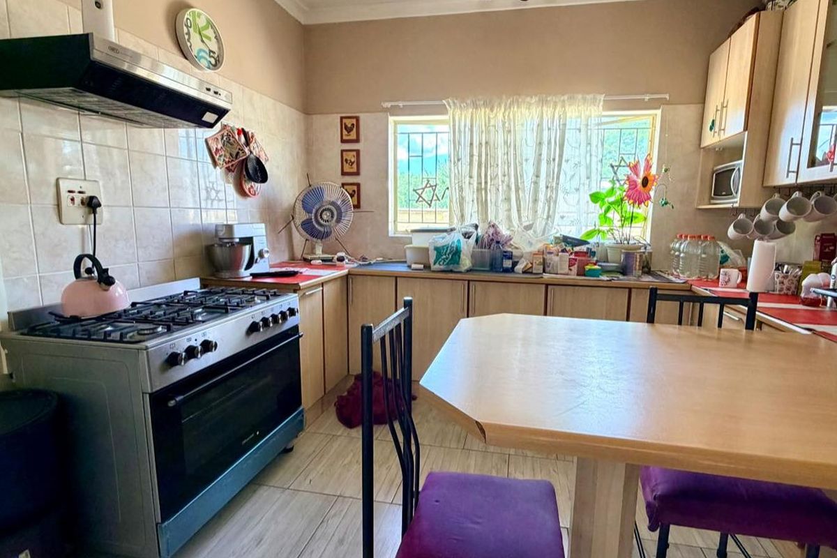 A functional kitchen featuring light wood cabinetry, a gas stove with extractor fan, tiled flooring, and a dedicated dining area.
