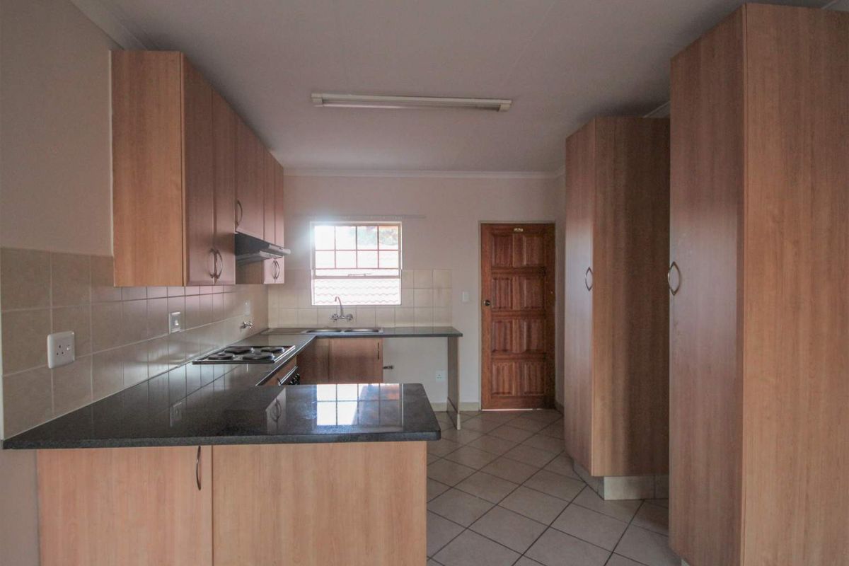 A functional kitchen featuring laminate cabinetry, granite countertops, an electric hob with extractor, and tiled flooring, offering a clean and practical workspace.