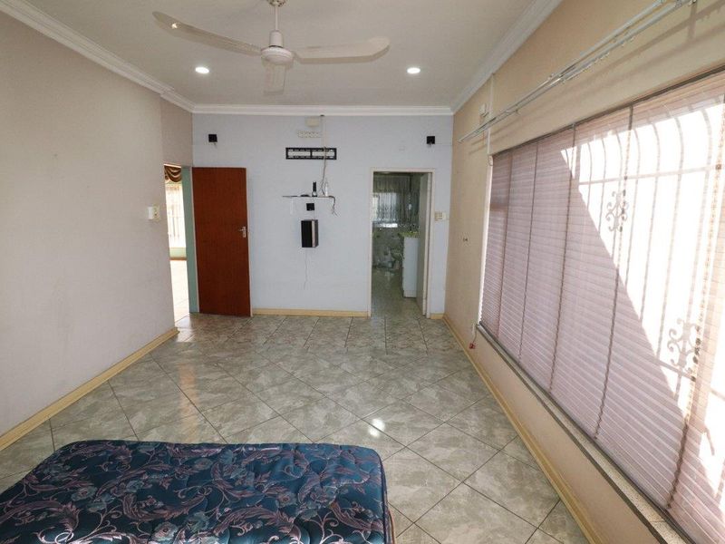 A spacious bedroom featuring tiled flooring, a ceiling fan, and security bars on the windows, offering a blank canvas for potential interior updates.