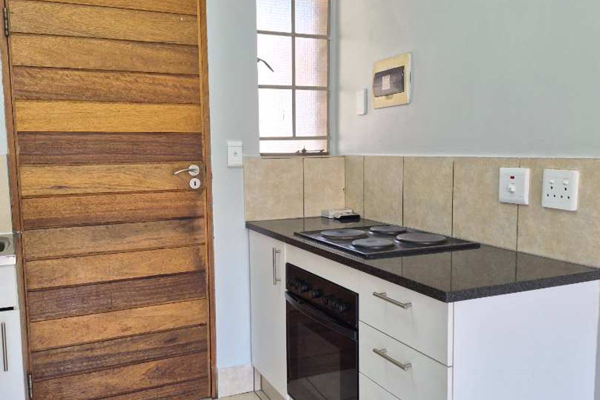 A compact kitchen featuring built-in oven, electric hob, granite countertops, tiled backsplash, and neutral tiled flooring, providing a functional and clean workspace.