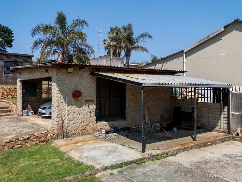 A detached, open-sided garage structure featuring stone masonry walls and a corrugated metal roof, situated on a concrete base.