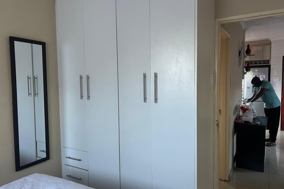 A bedroom featuring built-in white cabinetry with modern handles and a wall-mounted mirror, providing functional storage space.