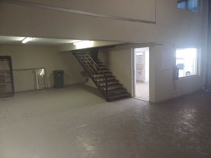 Spacious industrial utility area featuring a metal staircase, concrete flooring, and direct access to a small bathroom facility.