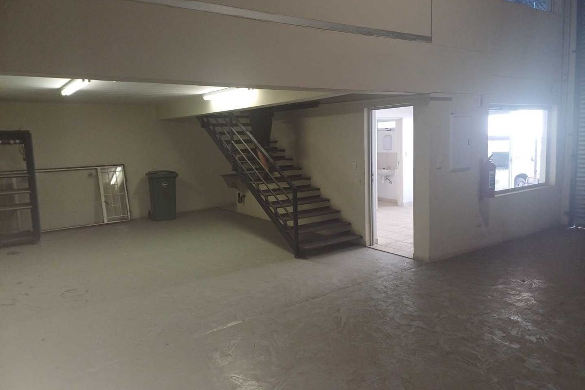 Spacious industrial utility area featuring a metal staircase, concrete flooring, and direct access to a small bathroom facility.