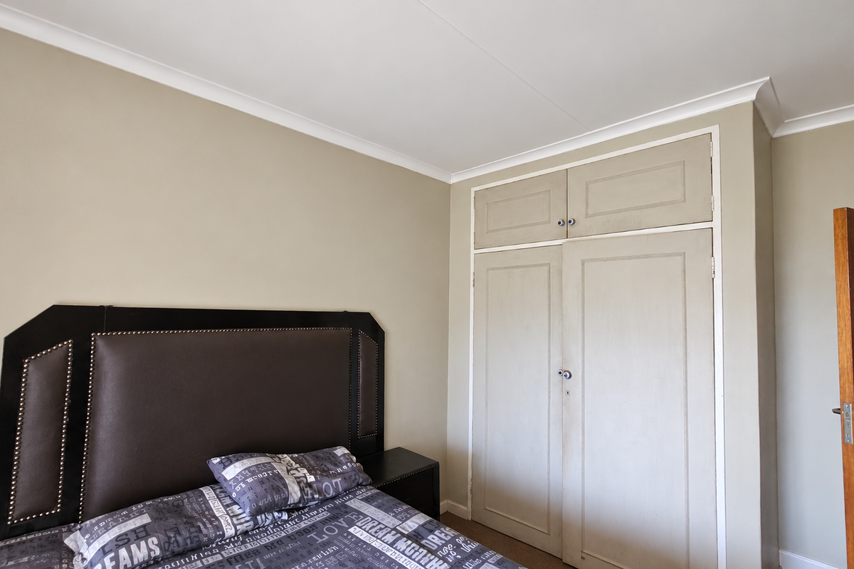 A bedroom featuring neutral wall tones, built-in cupboards with overhead storage, and classic cove cornicing.