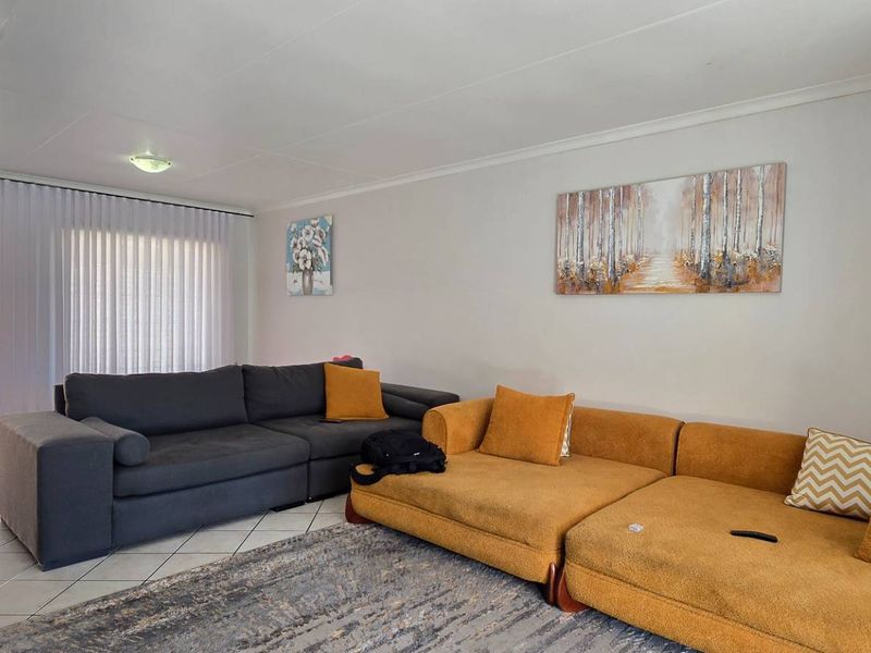 A spacious living room featuring tiled flooring, neutral walls, and a security gate leading to an outdoor area.
